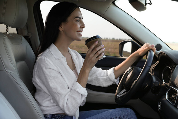 Beautiful young woman with cup of coffee driving her modern car - Foto, immagini