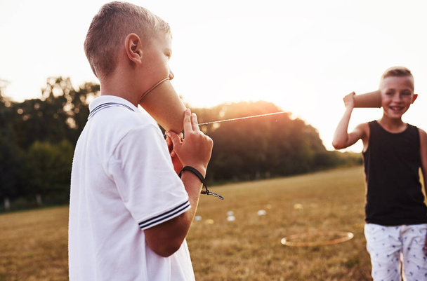 Two boys stands in the field and talking by using string can phone. - Fotoğraf, Görsel
