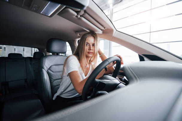 Feels tired. Girl in modern car in the salon. At daytime indoors. Buying new vehicle. - Foto, afbeelding