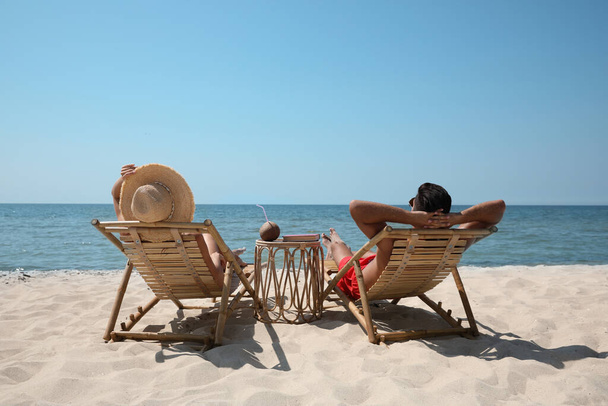 Couple resting in wooden sunbeds on tropical beach - Photo, image