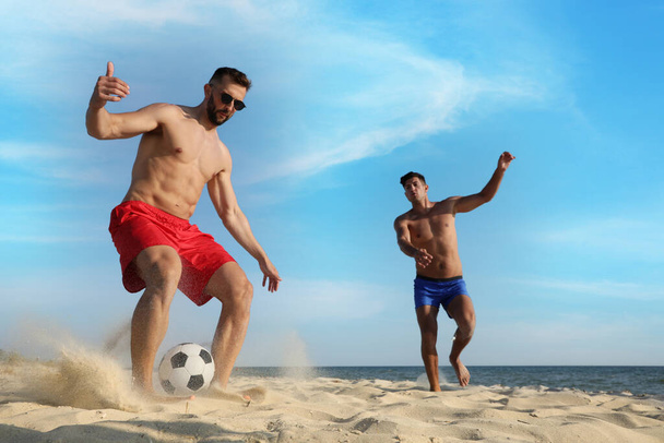Friends playing football on sandy beach near sea - Zdjęcie, obraz