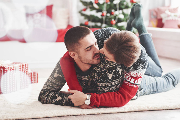 Geef me een kus. Mooi jong koppel liggend op de vloer van de woonkamer in nieuwjaar tijd met geschenkdozen. - Foto, afbeelding