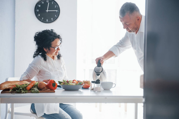 Forró tea. Férfi és felesége fehér ingben ételt készít a konyhában zöldségekkel. - Fotó, kép