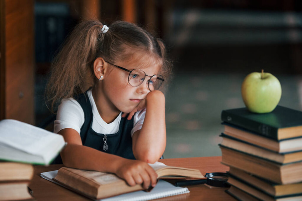 Bored and tired. Cute little girl with pigtails is in the library. Apple on the books. - Foto, Bild