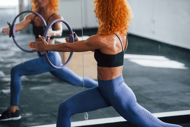 With special equipment. Sporty redhead girl have fitness day in gym at daytime. Muscular body type. - Fotoğraf, Görsel