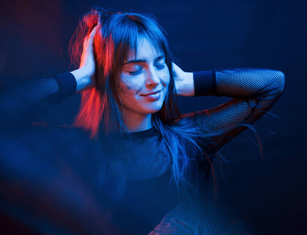 Standing in the lights. Studio shot in dark studio with neon. Portrait of young girl. - Фото, зображення