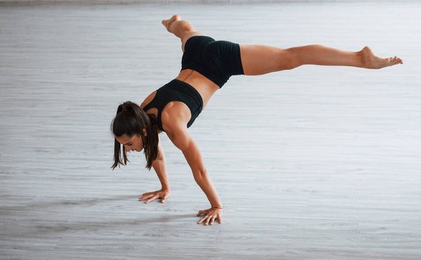 Doing hand stand. Young sporty woman in black clothes with slim body type in the healthy center doing exercises. - Foto, Imagem