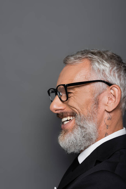 tattooed middle aged businessman in glasses smiling on grey - Foto, Bild