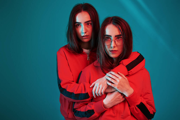 In red wear. Studio shot indoors with neon light. Photo of two beautiful twins. - Fotoğraf, Görsel