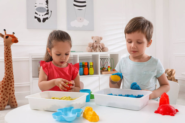 Cute little children playing with bright kinetic sand at table in room - Photo, Image
