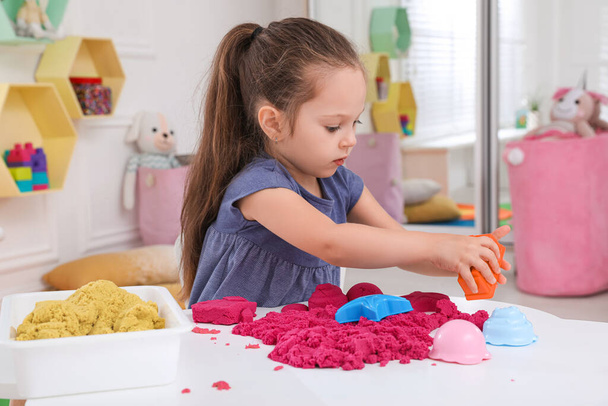 Cute little girl playing with bright kinetic sand at table in room - Foto, Bild