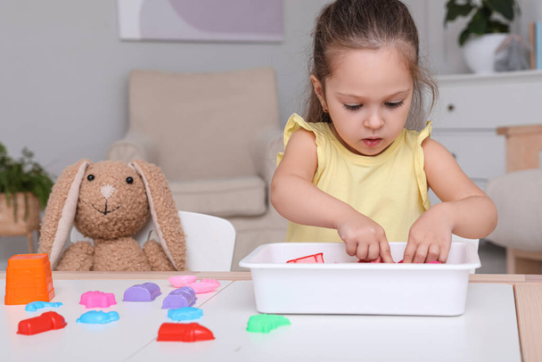 Cute little girl playing with bright kinetic sand at table in room - Foto, immagini
