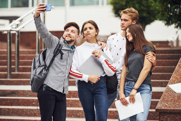 Standing and taking selfie. Group of young students in casual clothes near university at daytime. - Foto, Imagen