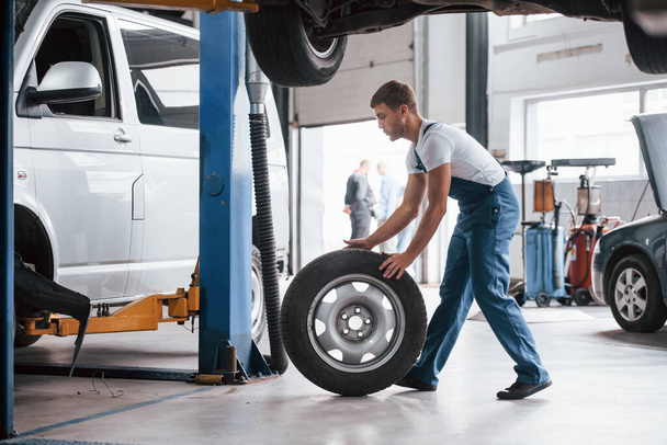 New tire. Employee in the blue colored uniform works in the automobile salon. - Foto, immagini