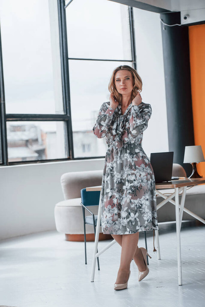 Cozy office. Businesswoman with curly blonde hair standing in room against window. - Foto, afbeelding
