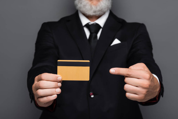 cropped view of bearded middle aged businessman in suit pointing at credit card isolated on grey - Photo, image