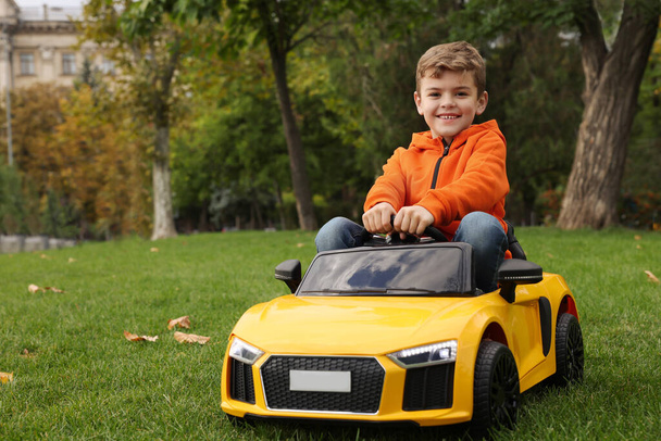 Cute little boy driving children's car in park. Space for text - Photo, image