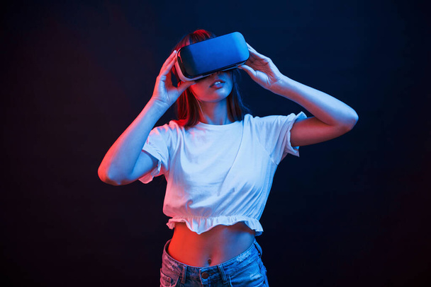 Amazing modern technologies. Young woman using virtual reality glasses in the dark room with neon lighting. - Foto, Bild