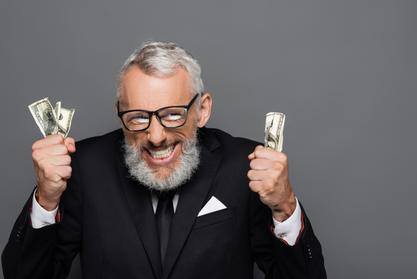 θετικός μεσήλικας επιχειρηματίας που διακρατεί τραπεζογραμμάτια δολαρίων απομονωμένα σε γκρίζα - Φωτογραφία, εικόνα