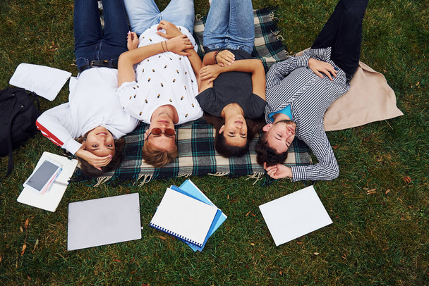 Having good rest. Group of young students in casual clothes on green grass at daytime. - Foto, immagini