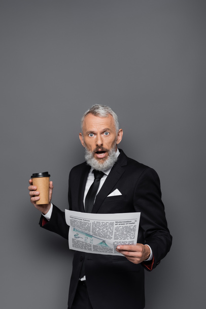 shocked middle aged businessman holding paper cup and newspaper on grey - Φωτογραφία, εικόνα