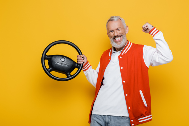 excited middle aged man in bomber jacket holding steering wheel on yellow - Foto, immagini