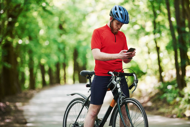 Chatting in internet. Cyclist on a bike is on the asphalt road in the forest at sunny day. - Photo, Image