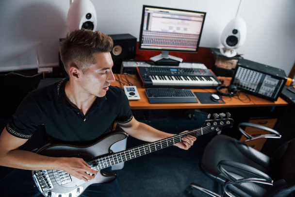 Young musician records bass guitar indoors in the studio. - Fotó, kép