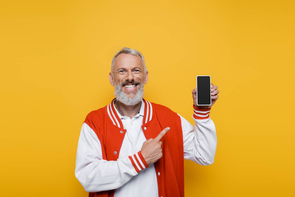 happy middle aged man pointing at smartphone with blank screen isolated on yellow  - Foto, Imagem