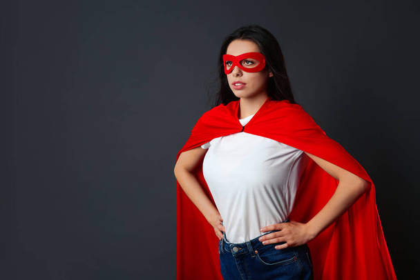Confident young woman wearing superhero cape and mask on grey background, space for text - Fotó, kép