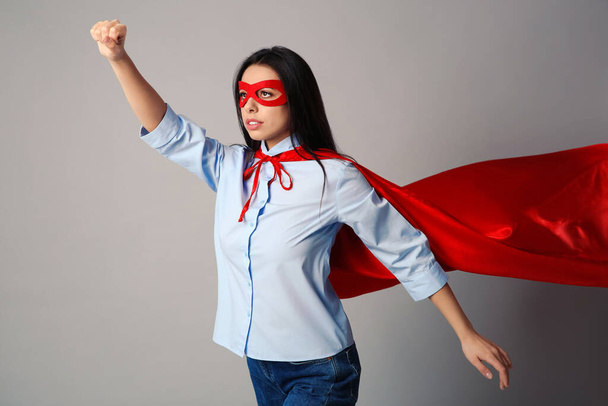 Confident young woman wearing superhero cape and mask on light grey background - Φωτογραφία, εικόνα
