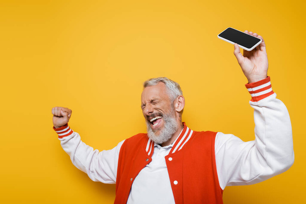 happy middle aged man with closed eyes holding smartphone with blank screen on yellow  - 写真・画像