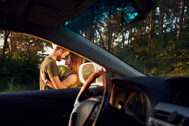 Vista desde el interior del coche. Volante, retrovisor lateral. Hermosa pareja joven pasar un buen rato en el bosque durante el día. - Foto, Imagen