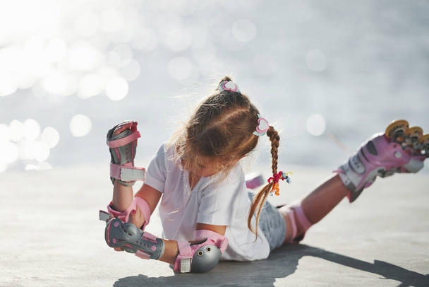 Lying down. Cute little girl with roller skates outdoors near the lake at background. - 写真・画像
