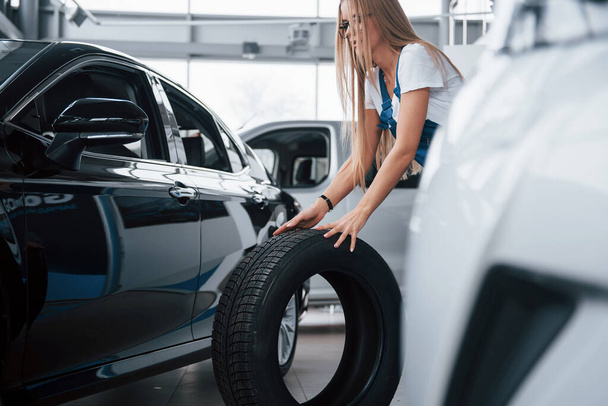 Doing her job well. Woman walks with brand new wheel to the car. Conception of repair. - Foto, imagen