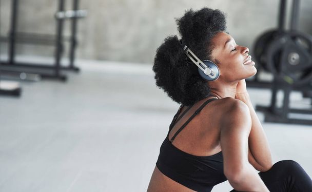 Such a lovely music. African american woman with curly hair and in sportive clothes have fitness day in the gym. - 写真・画像