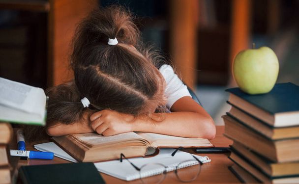 Sleeping on the table. Cute little girl with pigtails is in the library. Apple on the books. - Фото, зображення