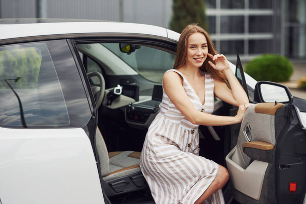 Smiling blonde sits in the white car. Business building behind. - Photo, Image