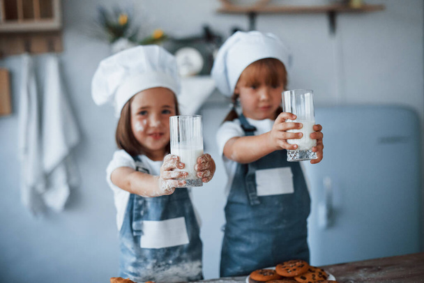 Wth glasses with milk. Family kids in white chef uniform preparing food on the kitchen. - Fotó, kép