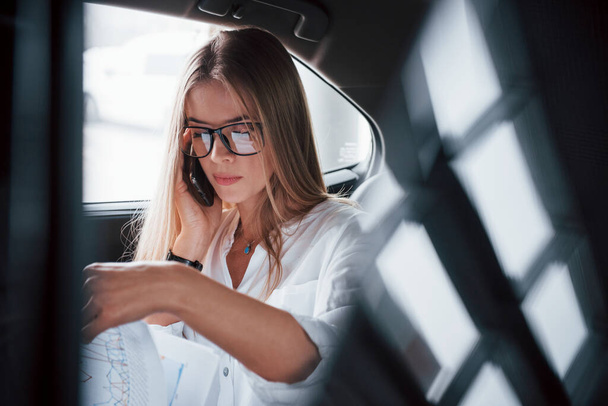Concentrated at work. Smart businesswoman sits at backseat of the luxury car with black interior. - Foto, imagen
