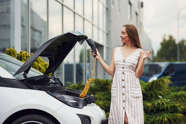 Wondering about new technology. Woman on the electric cars charge station at daytime. Brand new vehicle. - Zdjęcie, obraz