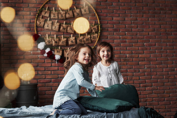 Young friends resting together. Little girls having fun on the bed with holiday interior at the background. - Foto, afbeelding
