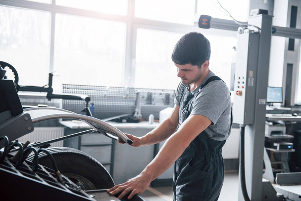 Let this machine do the job. Young man works with wheel's disks at the workshop at daytime. - Zdjęcie, obraz