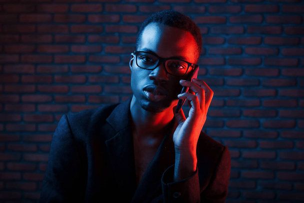 Having conversation by using phone. Futuristic neon lighting. Young african american man in the studio. - Zdjęcie, obraz