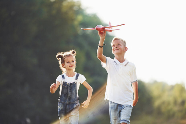 Girl and boy having fun outdoors with red toy airplane in hands. - Φωτογραφία, εικόνα