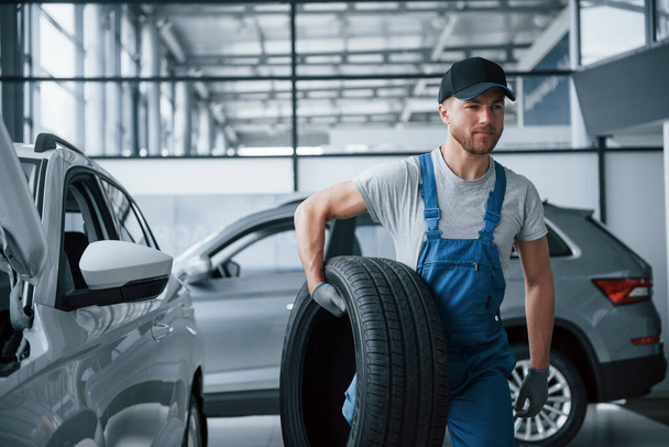 Thinking what to do next. Mechanic holding a tire at the repair garage. Replacement of winter and summer tires. - Foto, Imagem