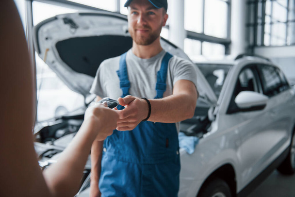 Take my keys. Woman in the auto salon with employee in blue uniform taking her repaired car back. - 写真・画像