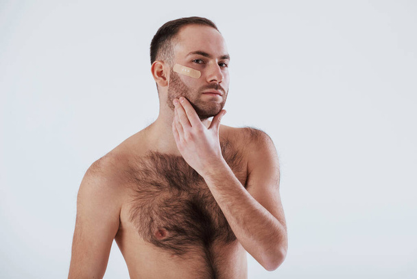 Here's what happening when you shave your beard not carefully. Man with bare chest stands against white background in the studio. - 写真・画像
