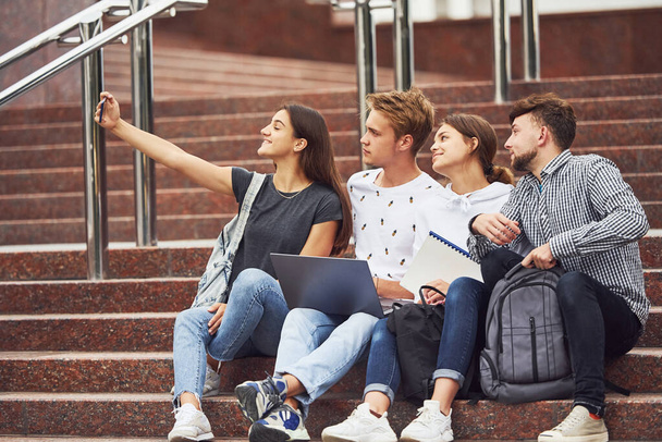 A tirar uma selfie. Grupo de jovens estudantes em roupas casuais perto da universidade durante o dia. - Foto, Imagem