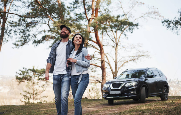 Peace and quiet. Embracing and enjoying the nature. Couple have arrived to the forest on their brand new black car. - Foto, imagen